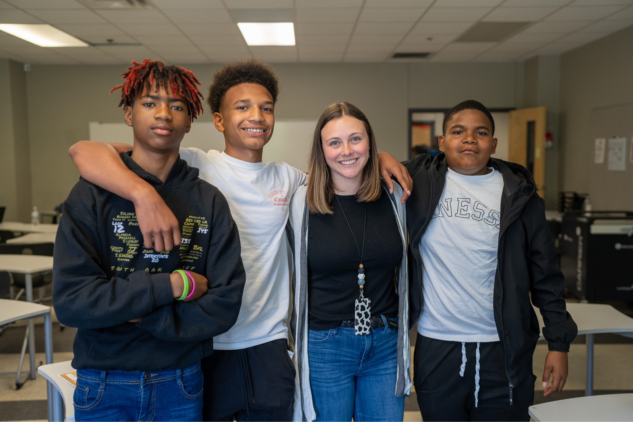 three male teens and a female teacher standing next to each other in a classroom