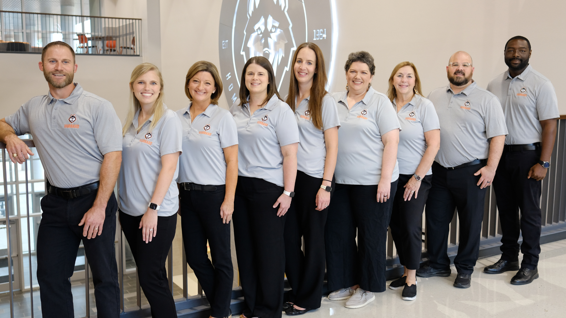 leadership staff standing on balcony with school logo sign on wall in background