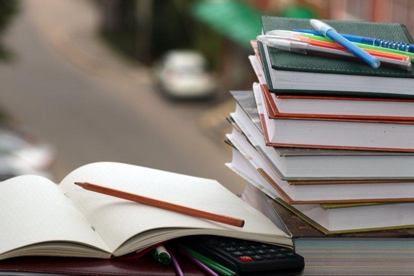 stack of books topped with pencils beside and open notepad