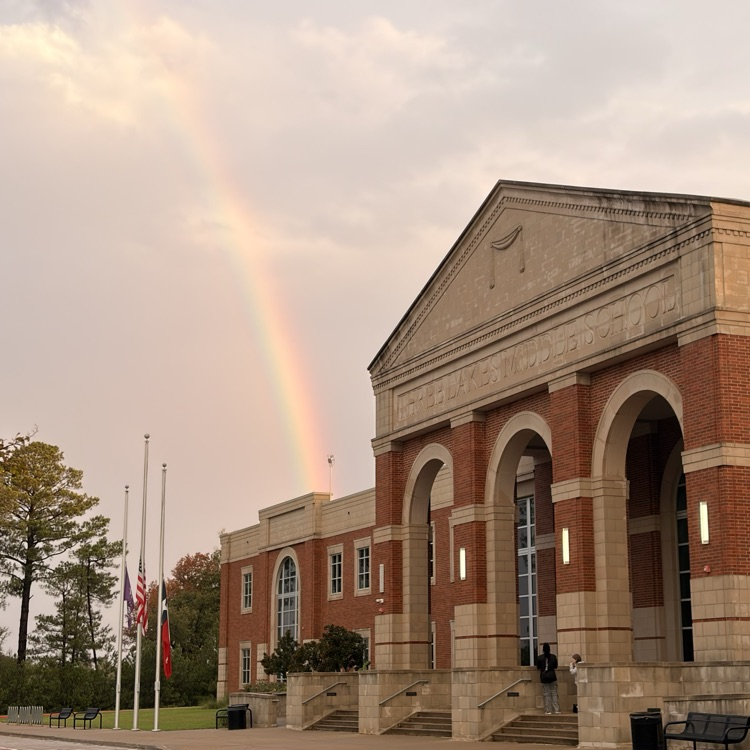 A rainbow above a building. It has arched windows, pillars, and steps leading to the entrance.