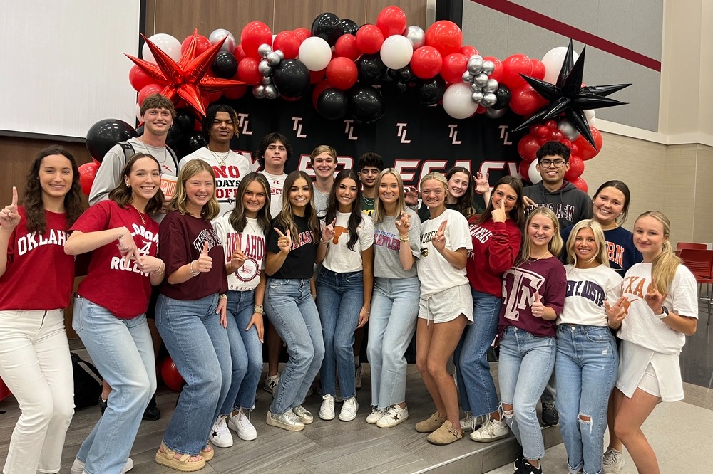 A group of people wearing maroon and white tops pose for a photo in front of a colorful balloon arch.