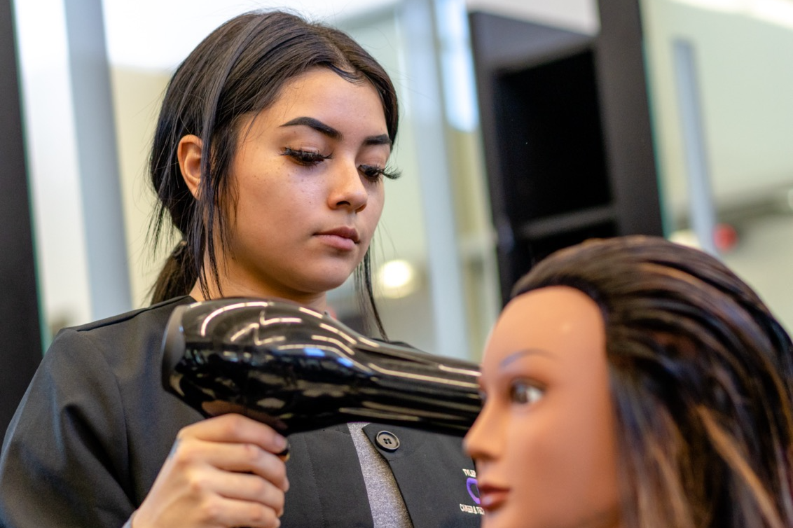 student using hair dryer on practice wig