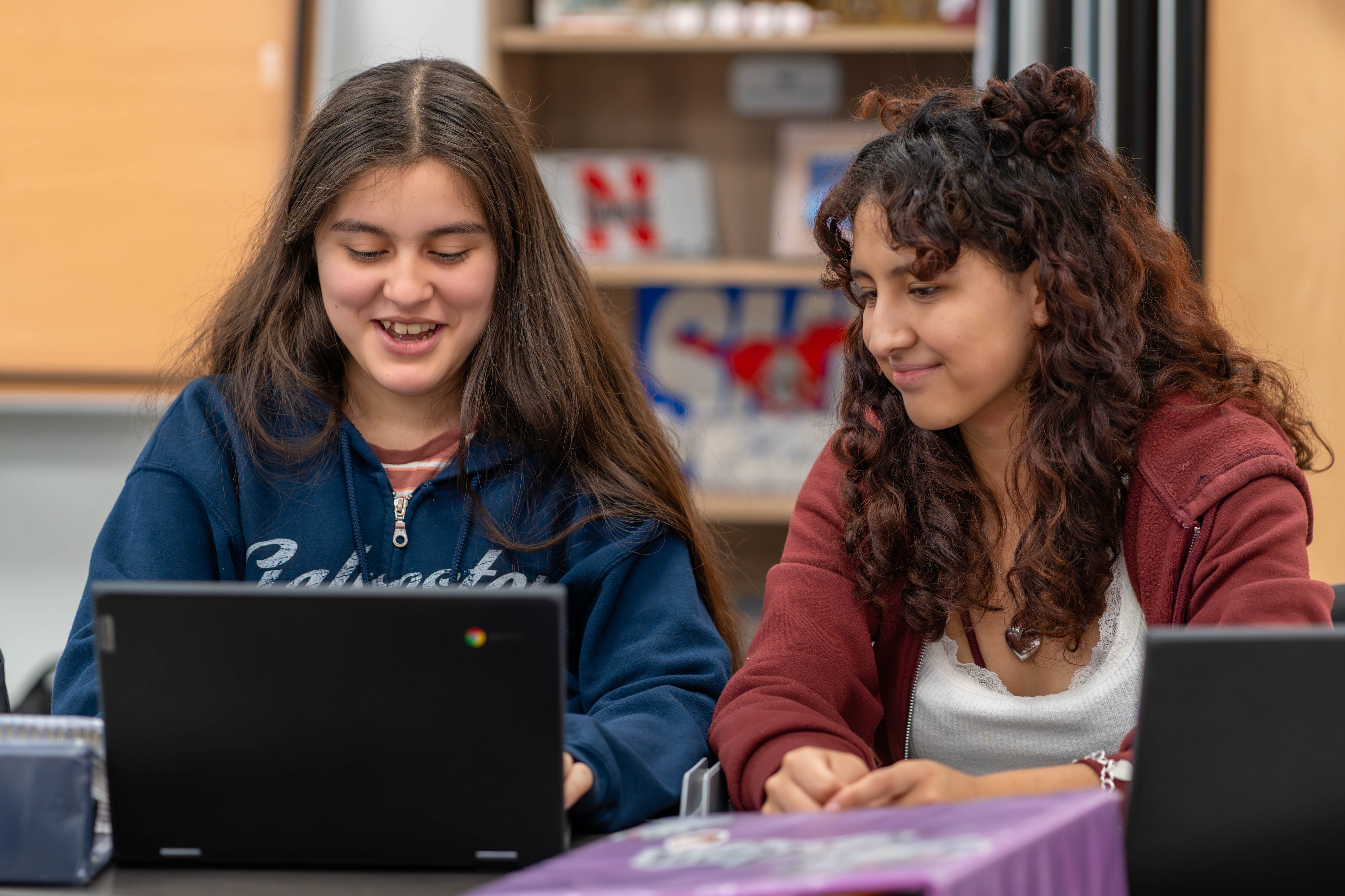 two teen girls working on laptop and smiling