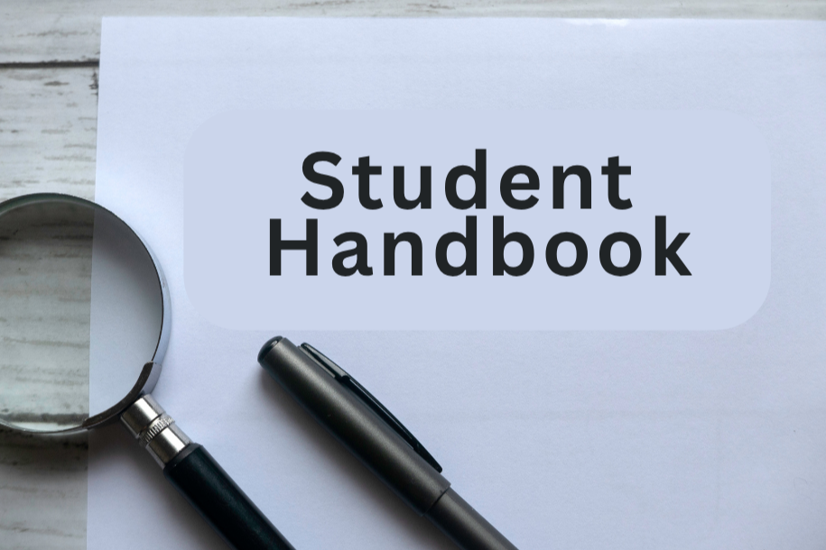 A white sheet of paper labeled "Student Handbook" with a magnifying glass and a pen on a wooden surface.