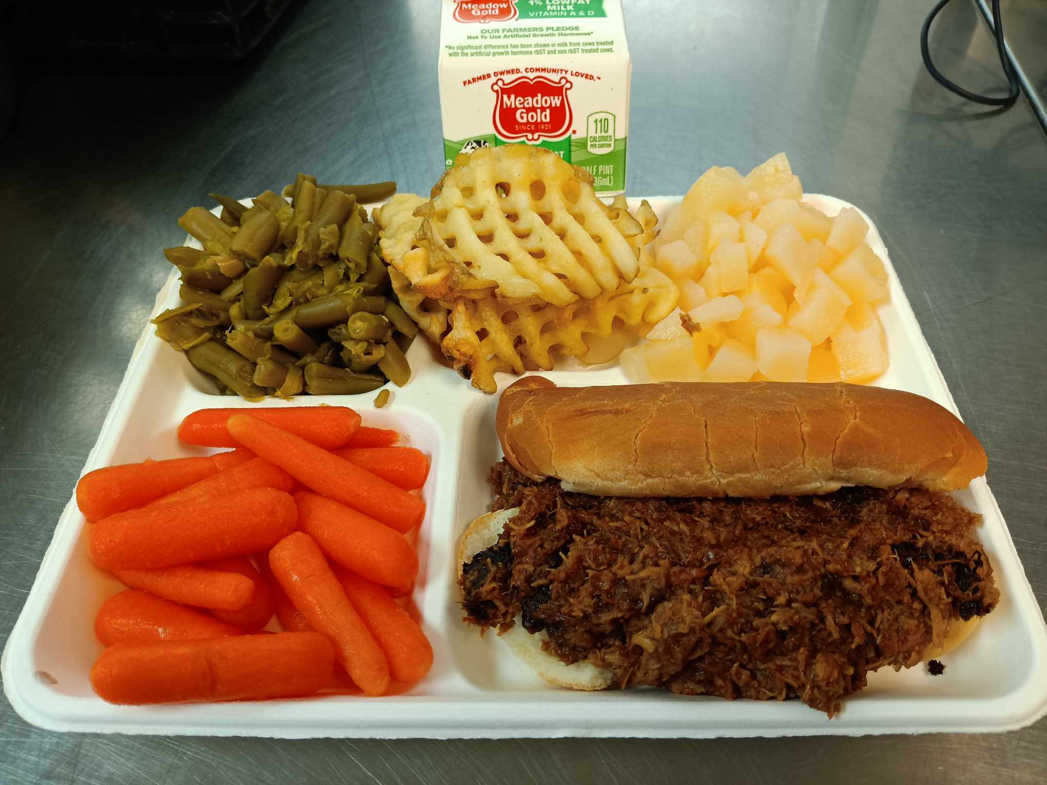 Pulled pork sandwich, waffle fries, green beans, pears, carrots, and milk