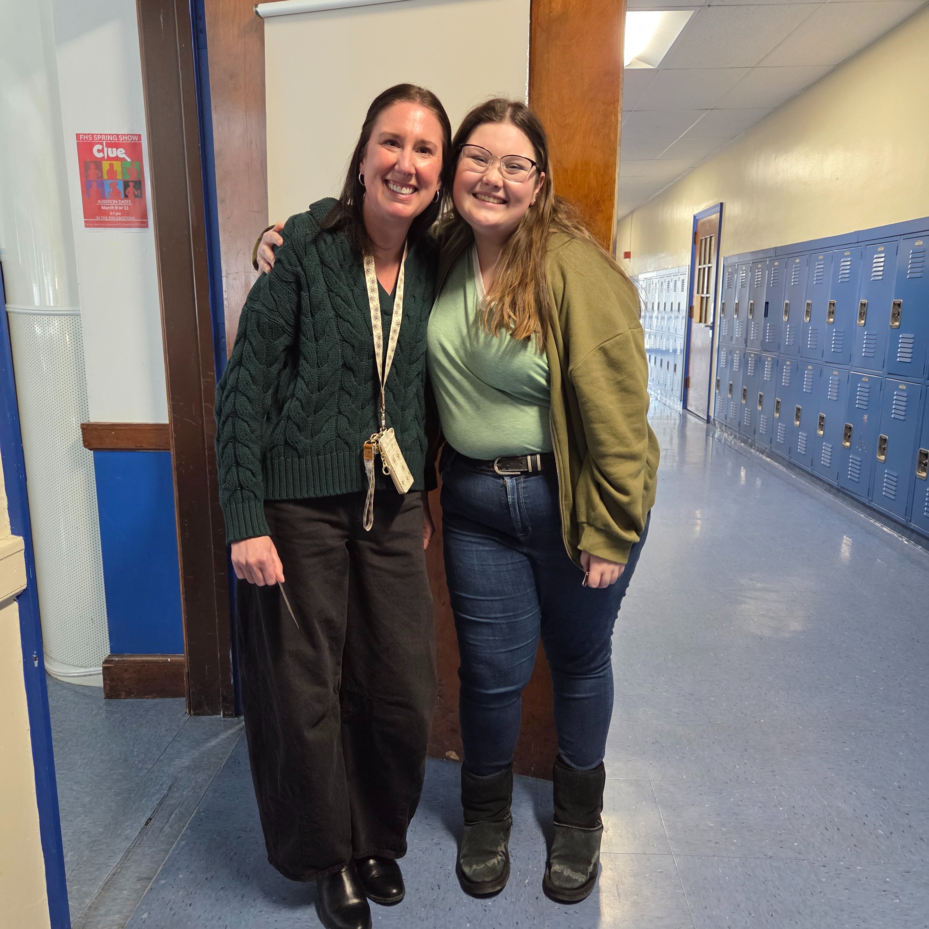Two women pose for a photo in a school hallway, with lockers visible in the background.
