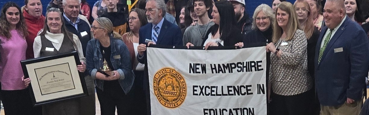 A large crowd gathered in a gymnasium, with some individuals holding banners, while a person is capturing the scene.