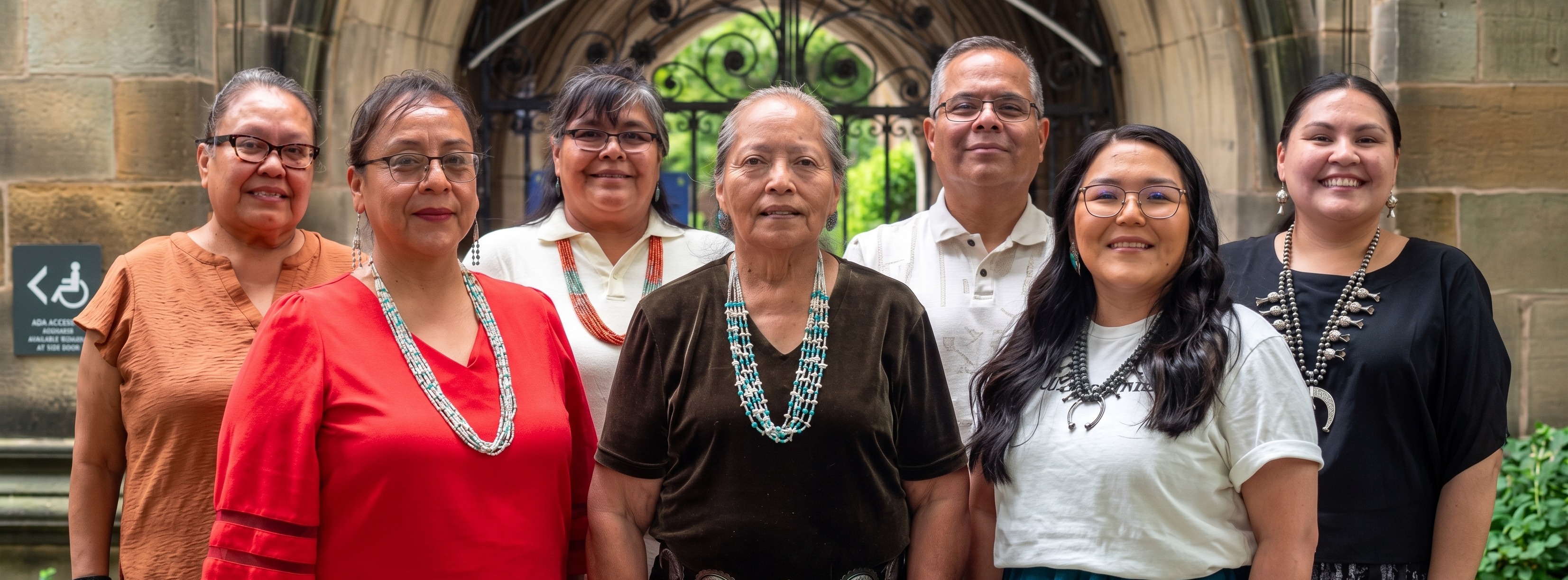 Nine people wearing various jewelry pose for a photo in front of a building.