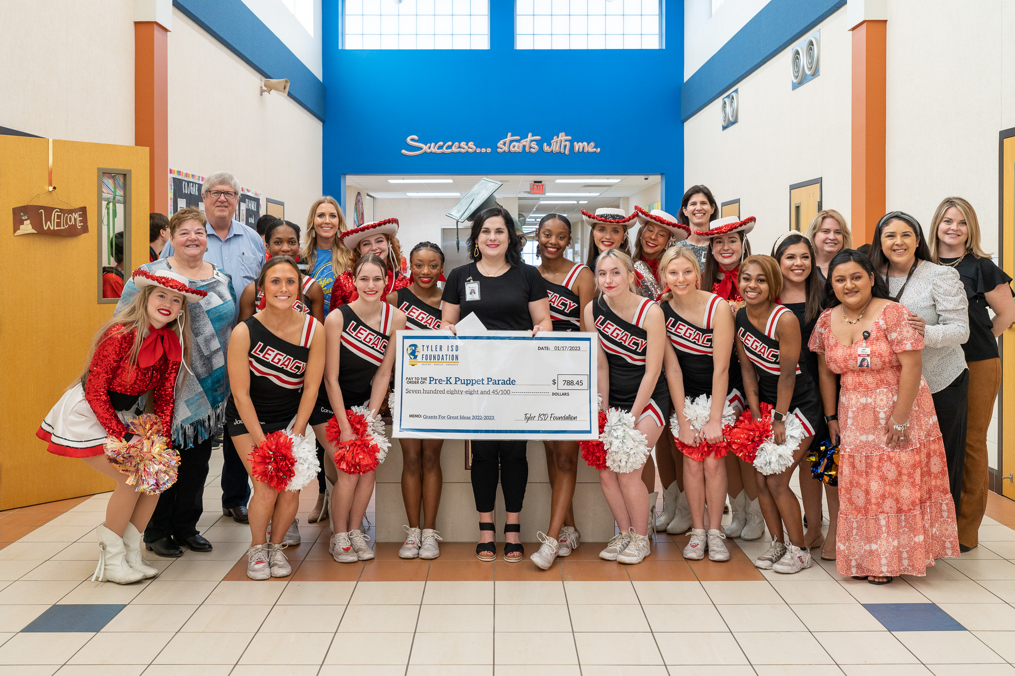 group of people standing in a hallway holding a giant check