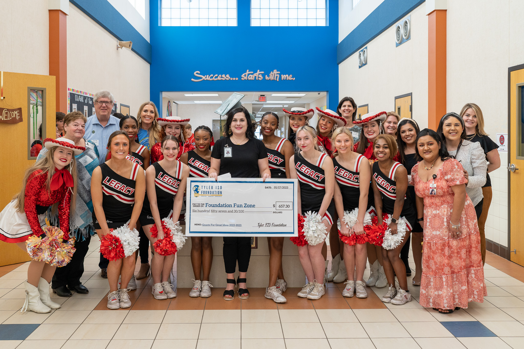 group of people standing in a hallway holding a giant check