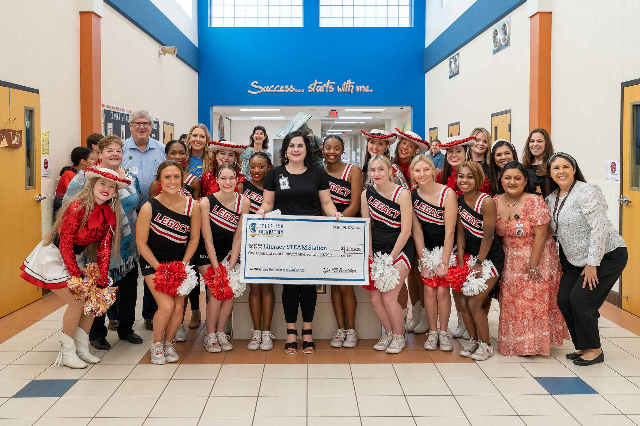 group of people standing in a hallway holding a giant check