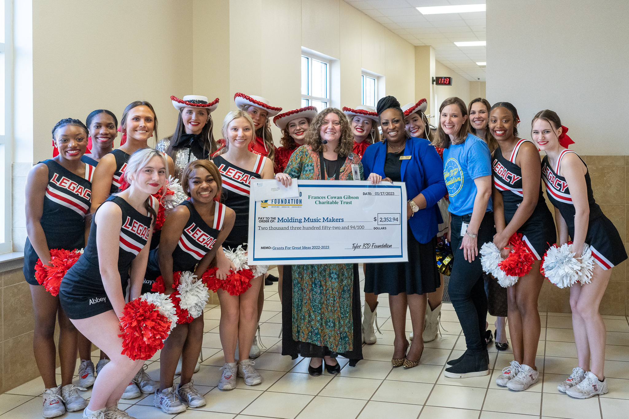 group of people standing in a hallway holding a giant check