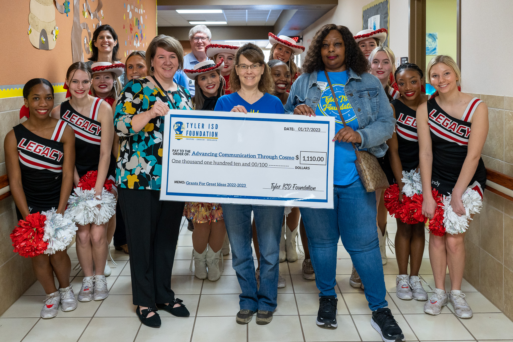 group of people standing in a hallway holding a giant check