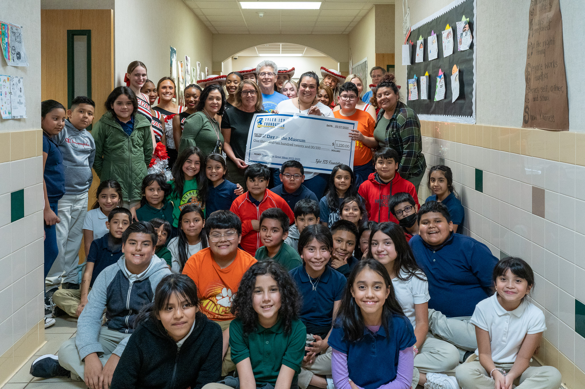 group of people standing in a hallway holding a giant check