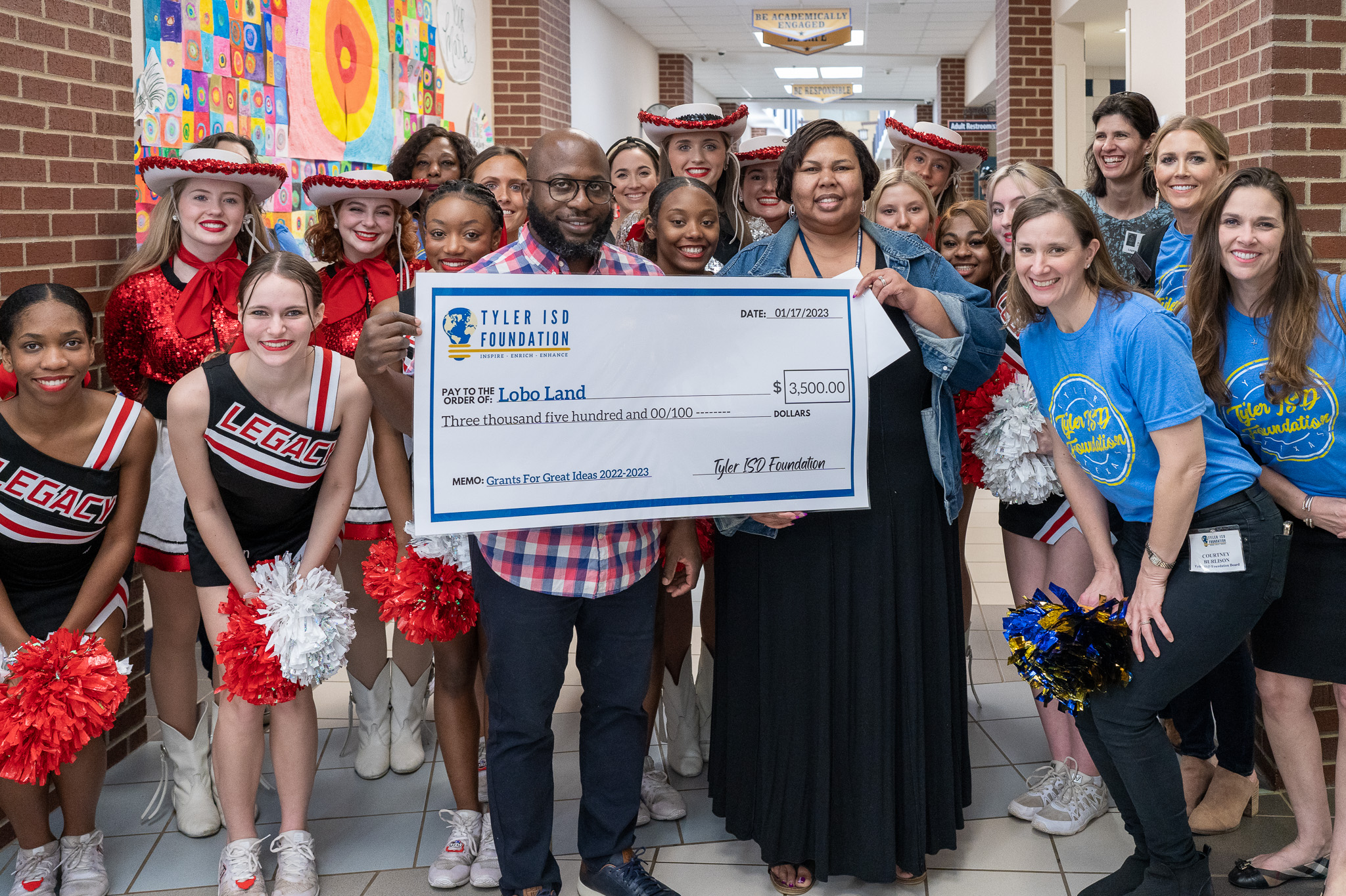 group of people standing in a hallway holding a giant check