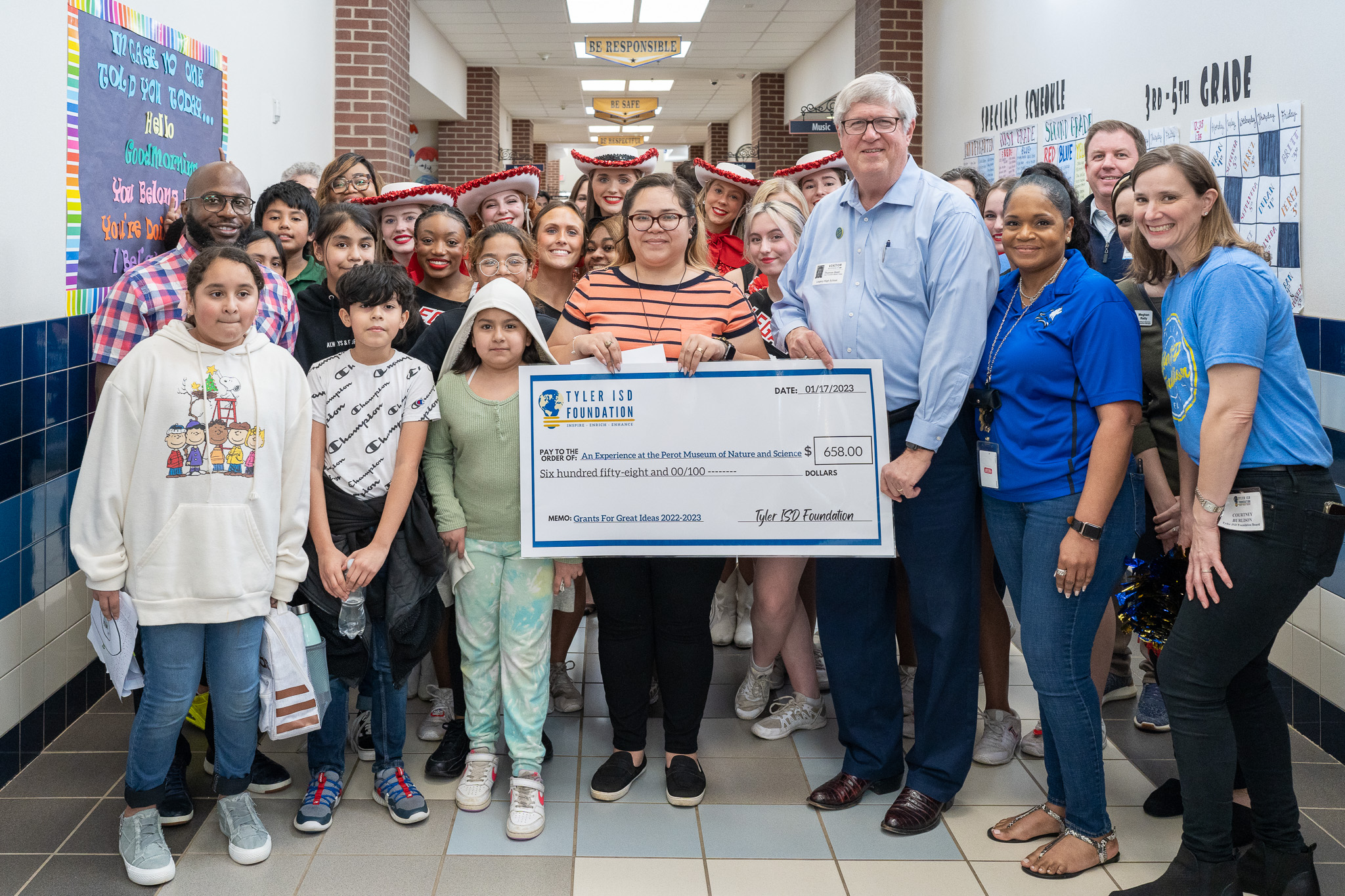 group of people standing in a hallway holding a giant check