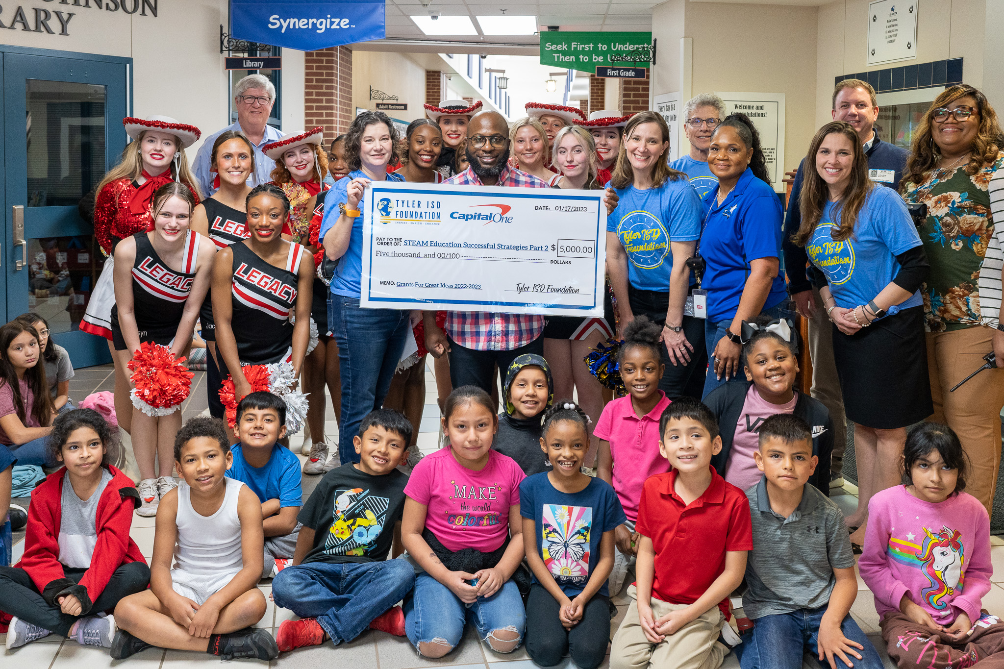 group of people standing in a hallway holding a giant check