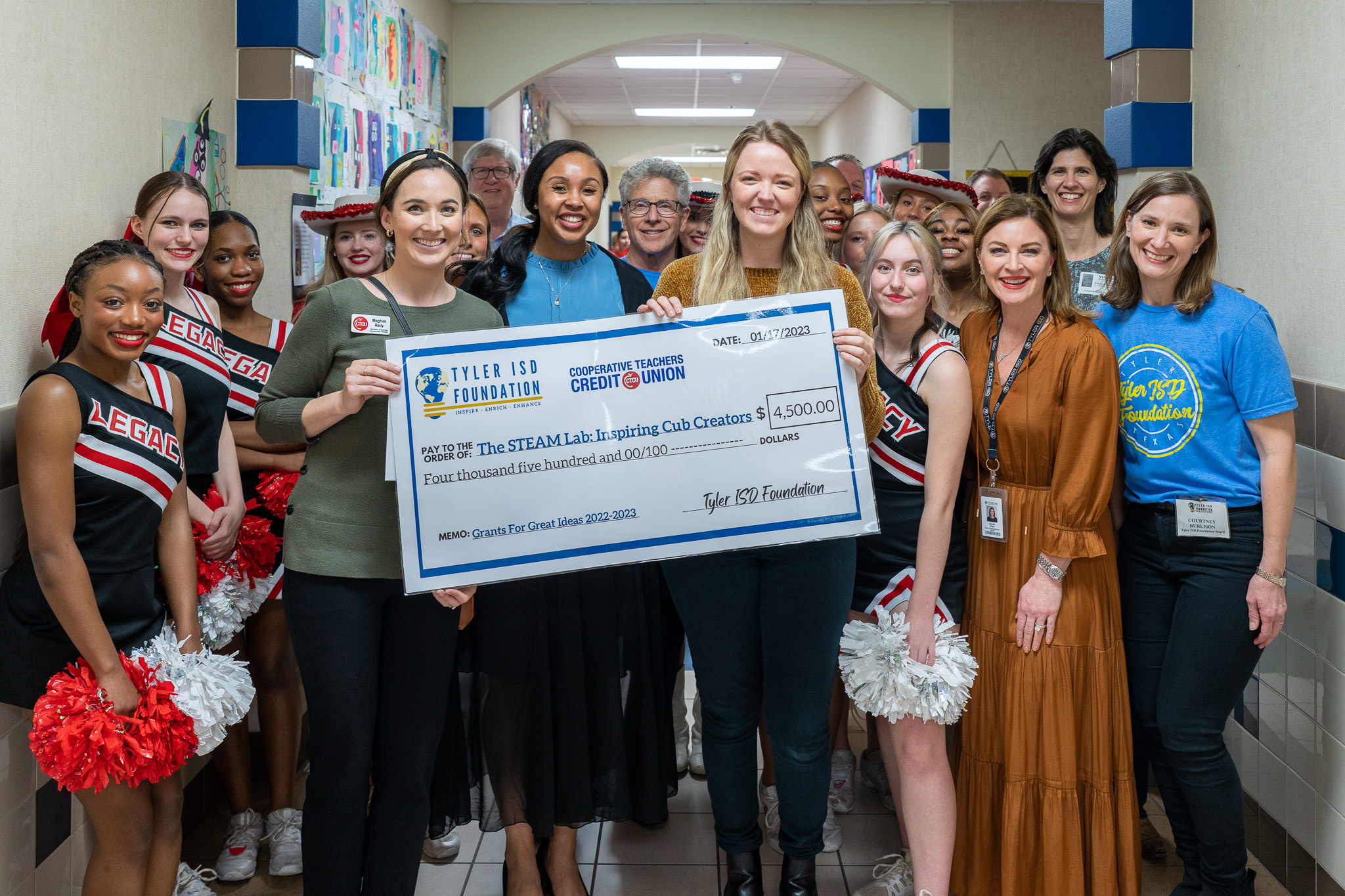 group of people standing in a hallway holding a giant check