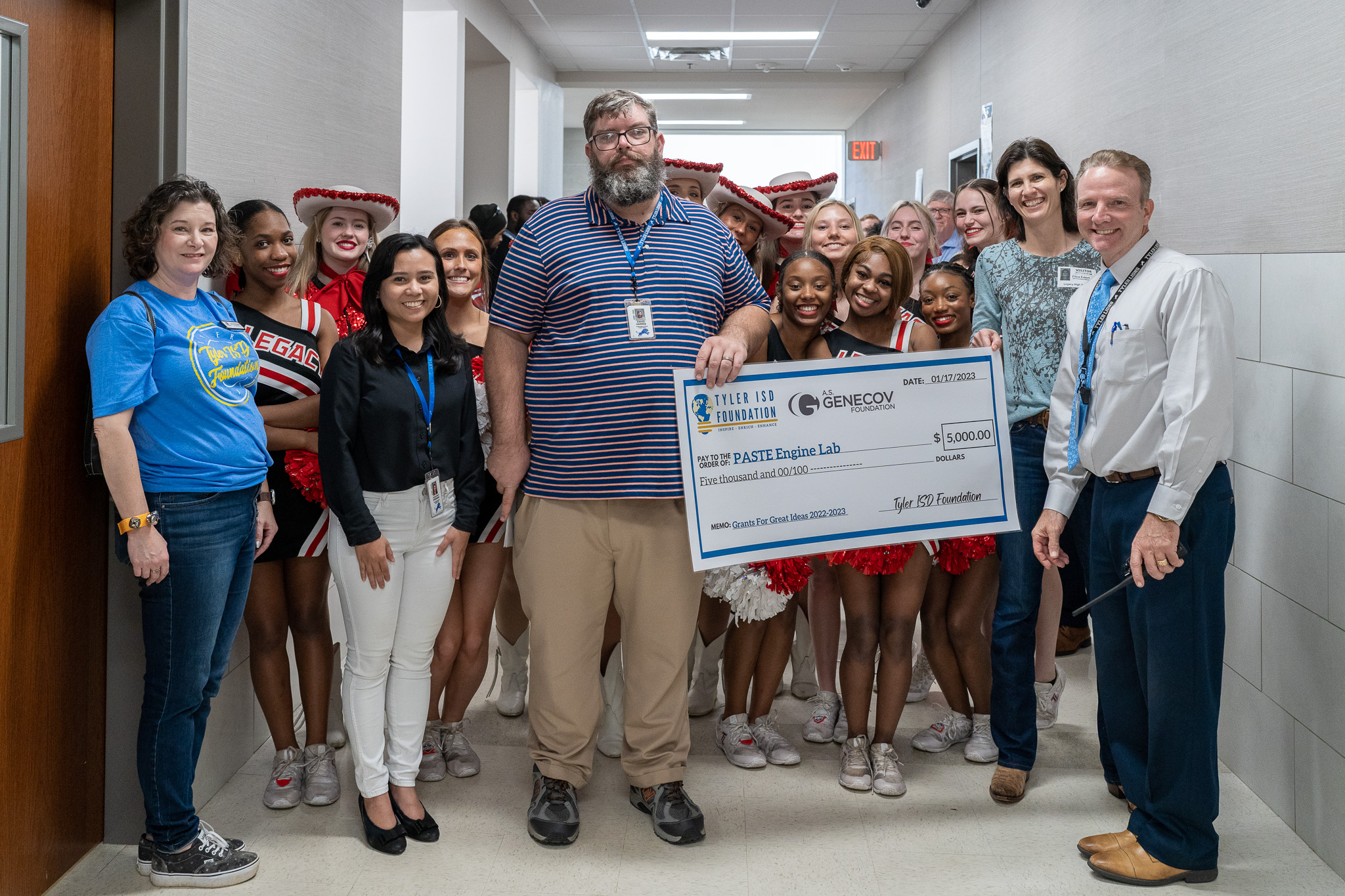 group of people standing in a hallway holding a giant check