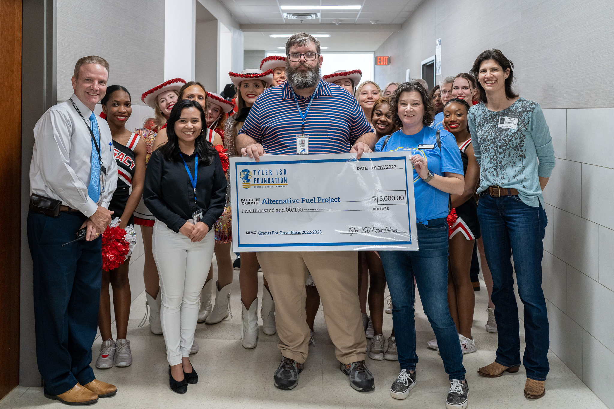 group of people standing in a hallway holding a giant check