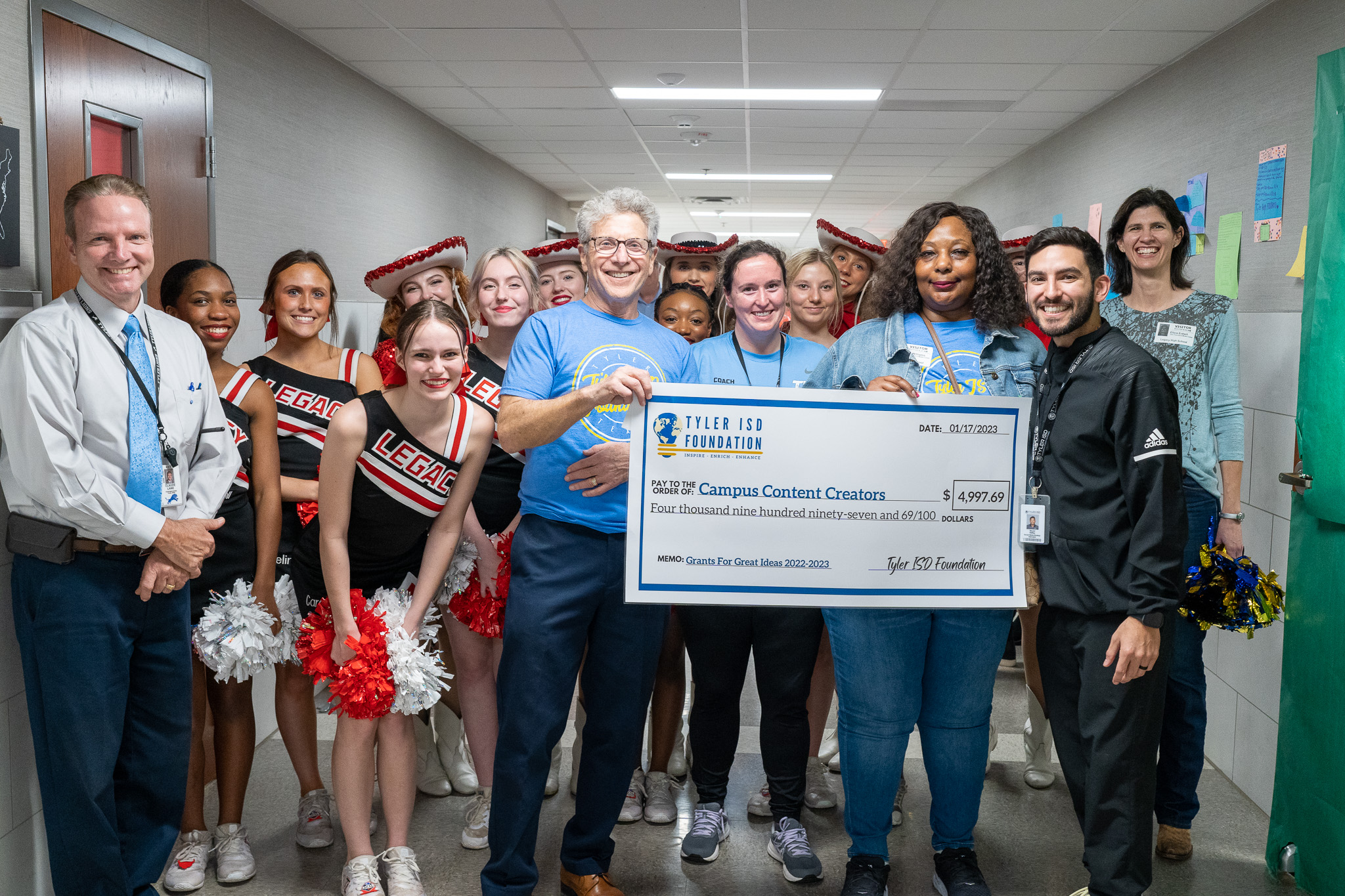 group of people standing in a hallway holding a giant check