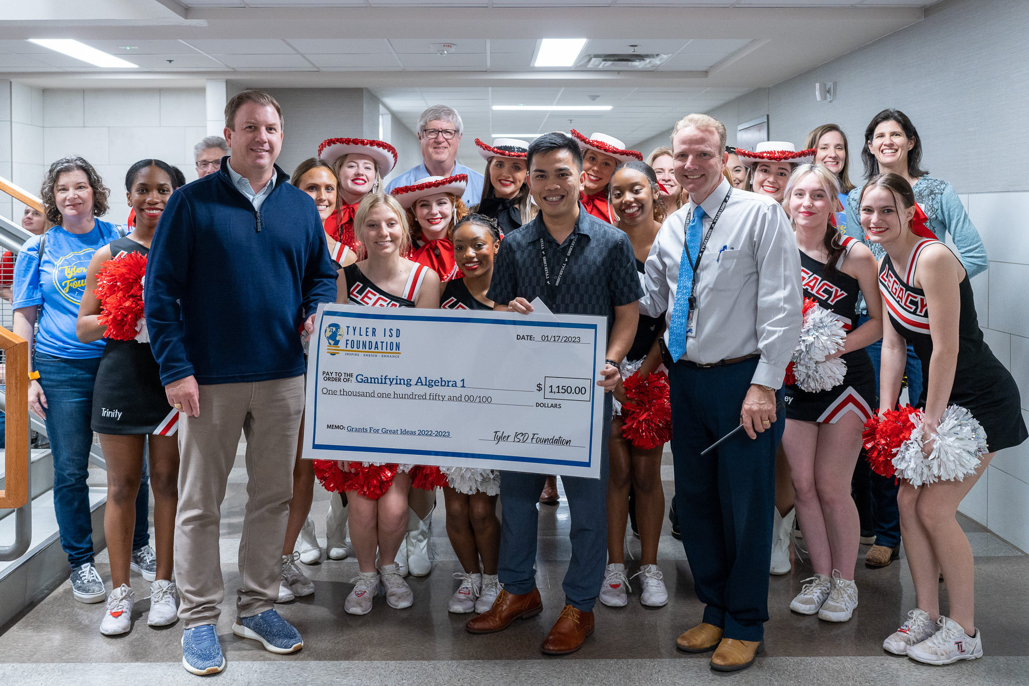 group of people standing in a hallway holding a giant check