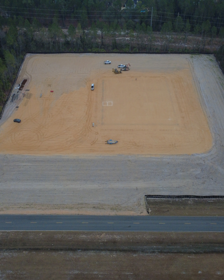 Aerial view of a construction site with a large area of sand and a road on the lower right.