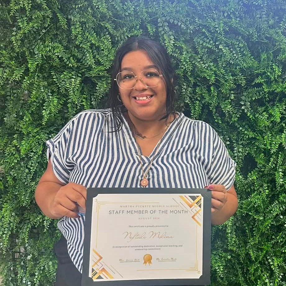 A woman holds a framed certificate in front of a green wall with "Martha Bucket" glowing in blue.