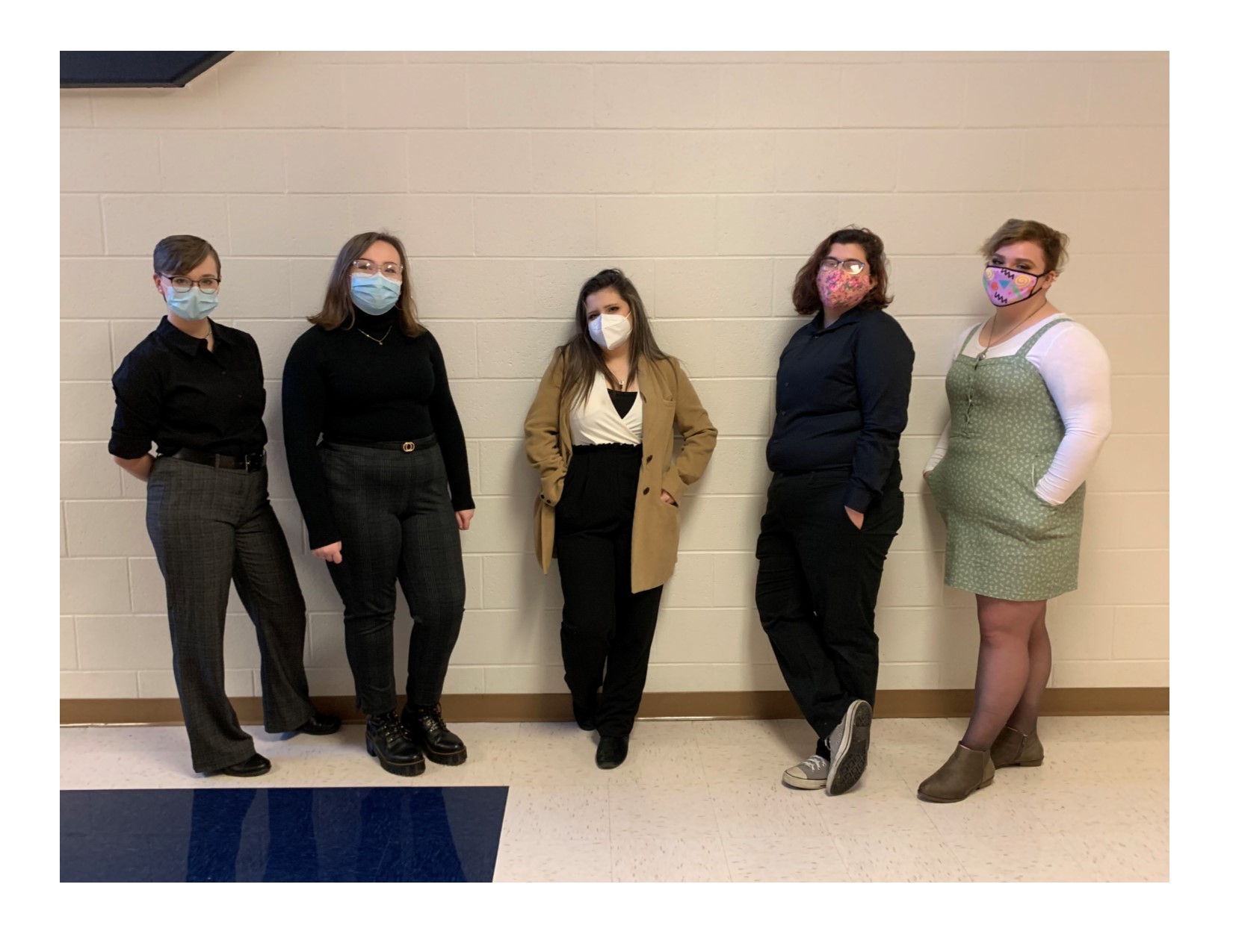 5 students standing against a white wall in business casual wearing masks
