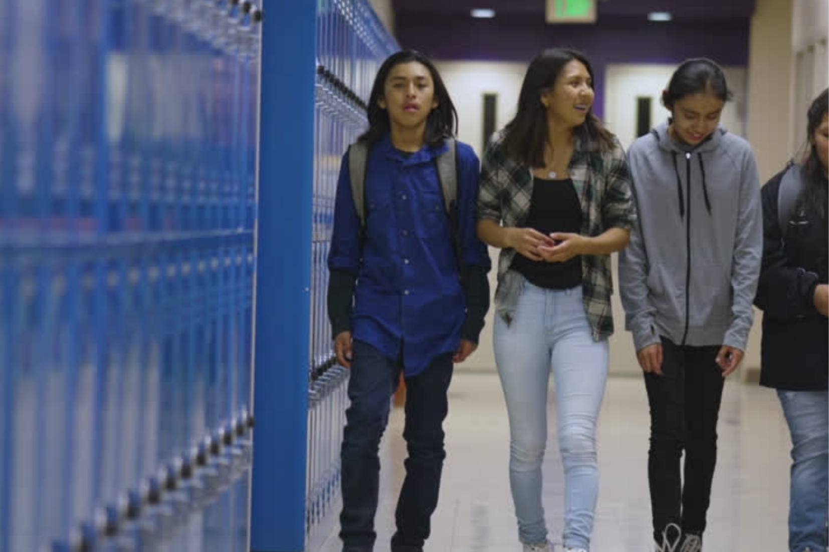 middle schoolers walk down the hallway with blue lockers on one side