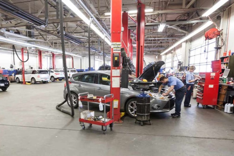 A vehicle repair shop with multiple mechanics working on a car under a lift with tools and equipment.