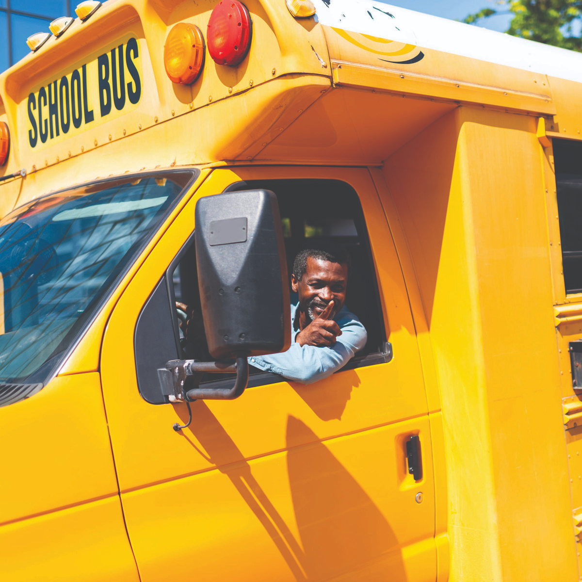 Bus driver leaning out a window of a school bus waving