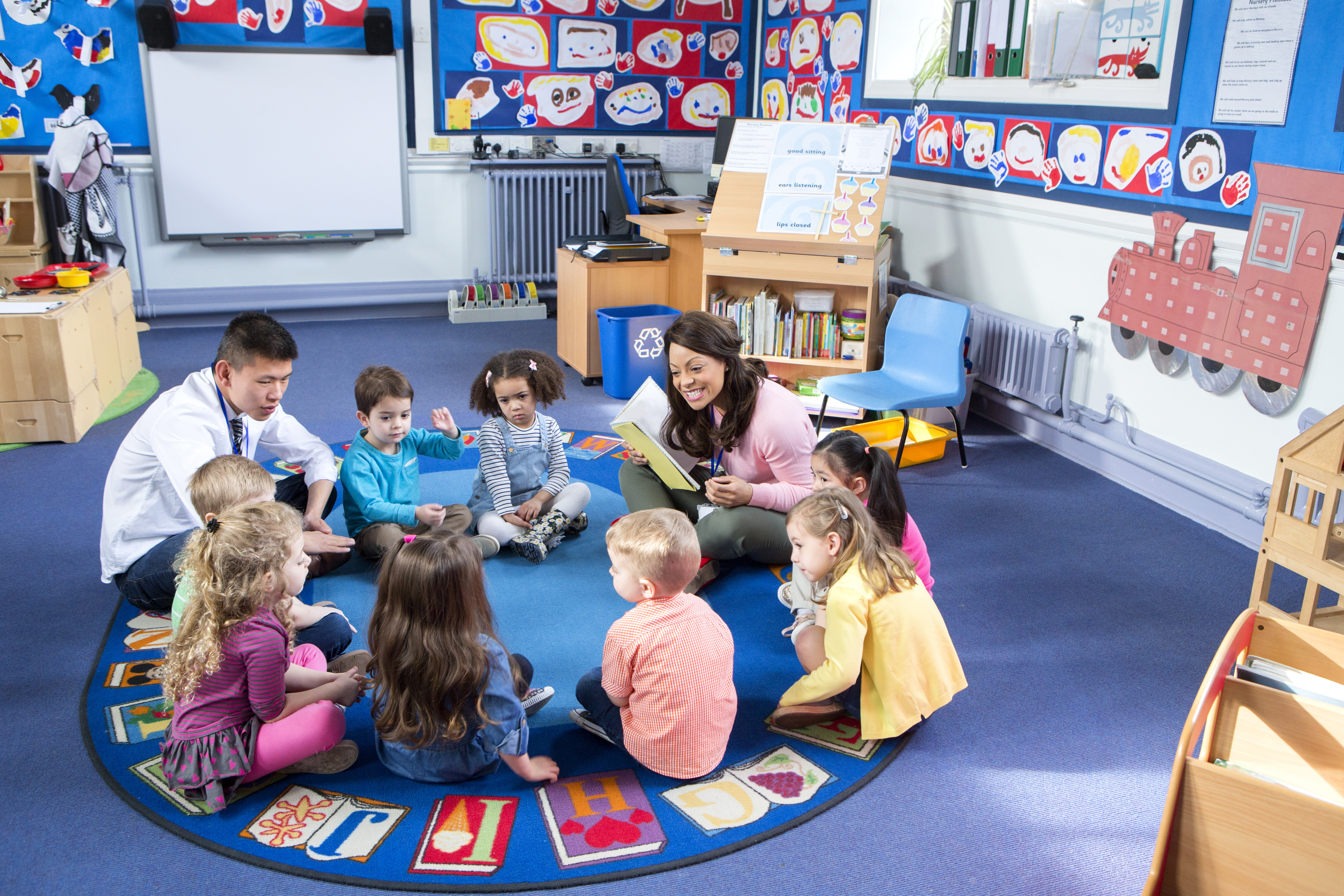 A teacher and volunteer reading to children in a circle.