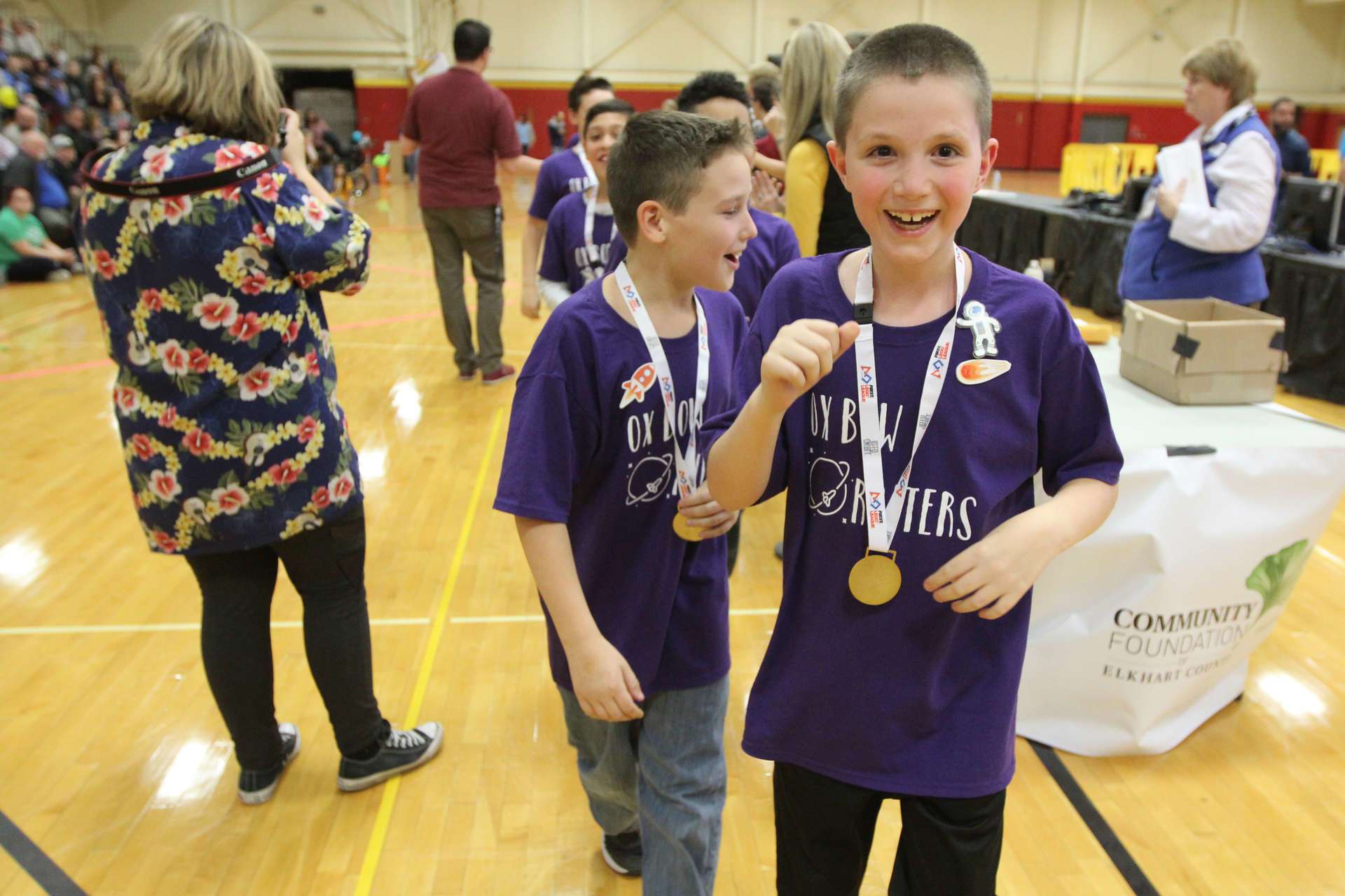 Student in a gym holding a medal with several people in the background