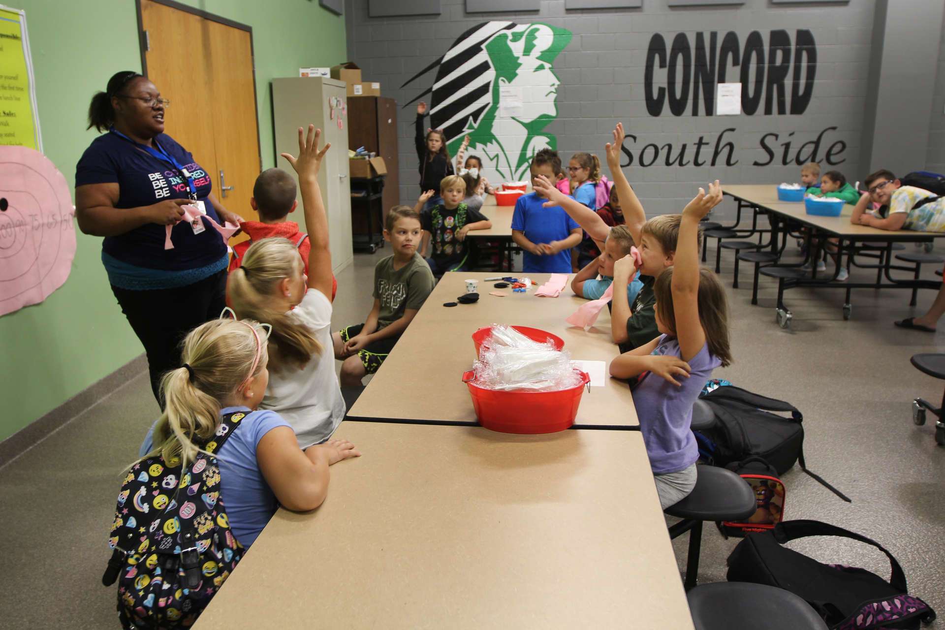 Students sitting at a long table together, some raising their hands