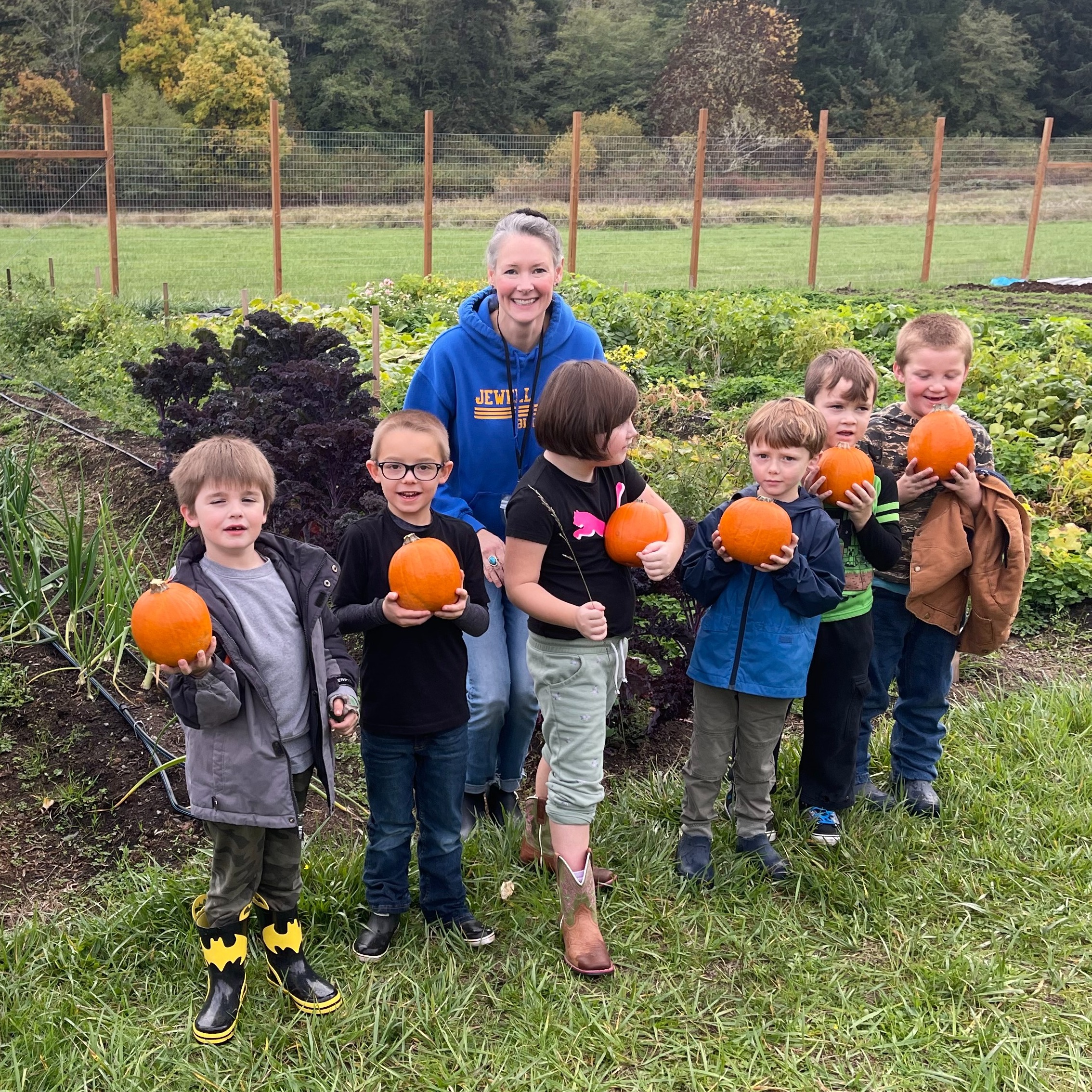 Six students with their teacher holding small orange pumpkins that they picked.