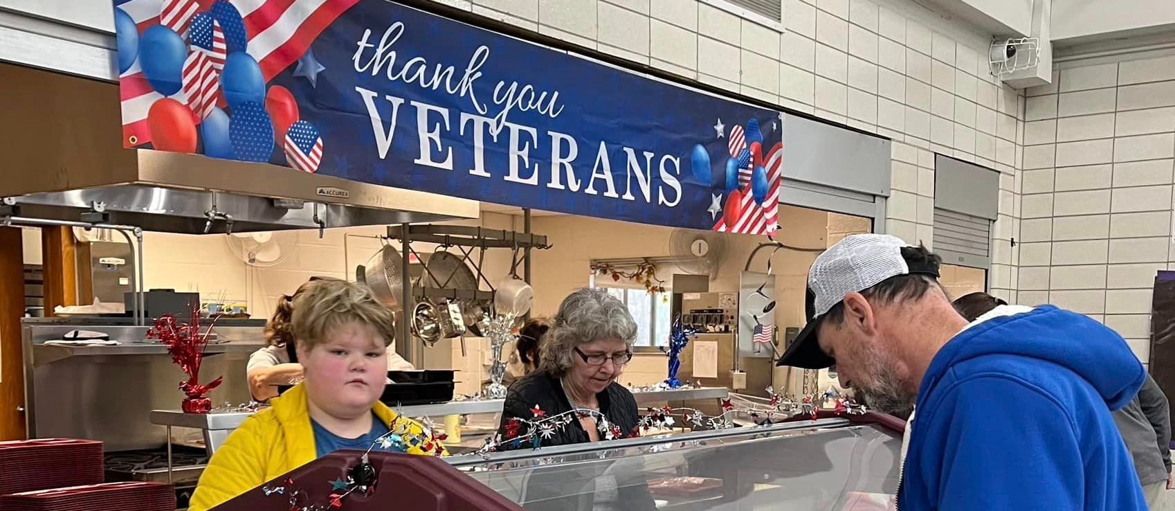 Veterans  and students get fill trays in the lunch line under a banner saying, "Thank You Veterans"