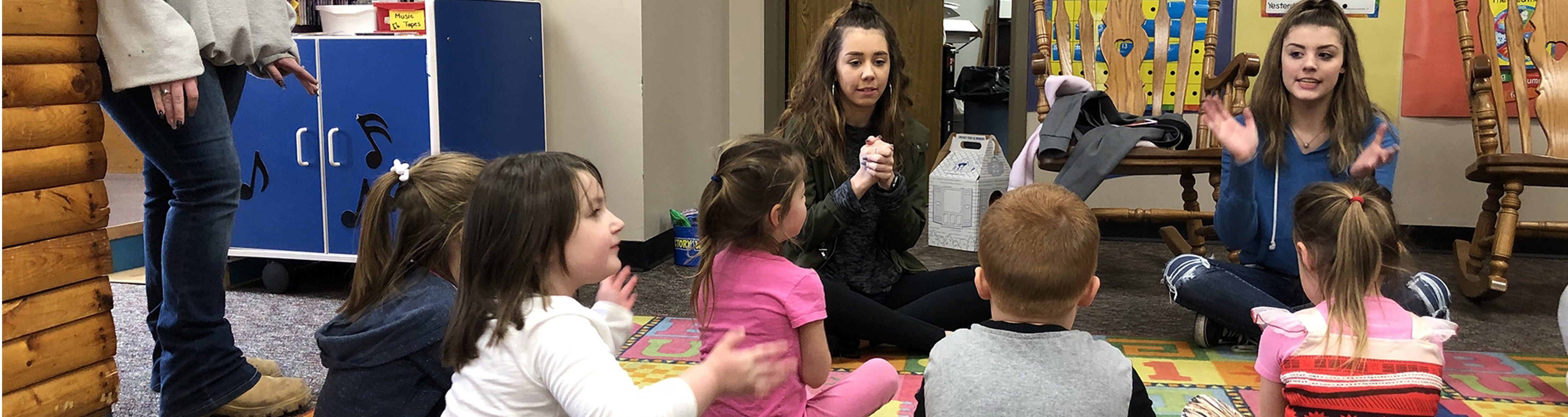 Two teachers sitting on the floor with an early childhood group