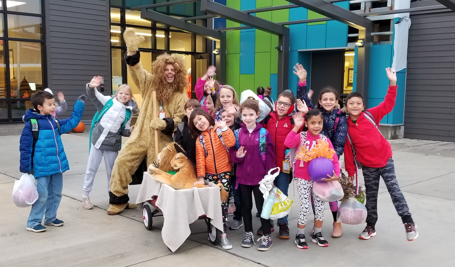 students waving in front of school with the principal who is dressed as a lion mascot
