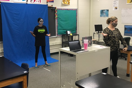 student with face painted standing in front of blue screen with teacher rehearsing for musical
