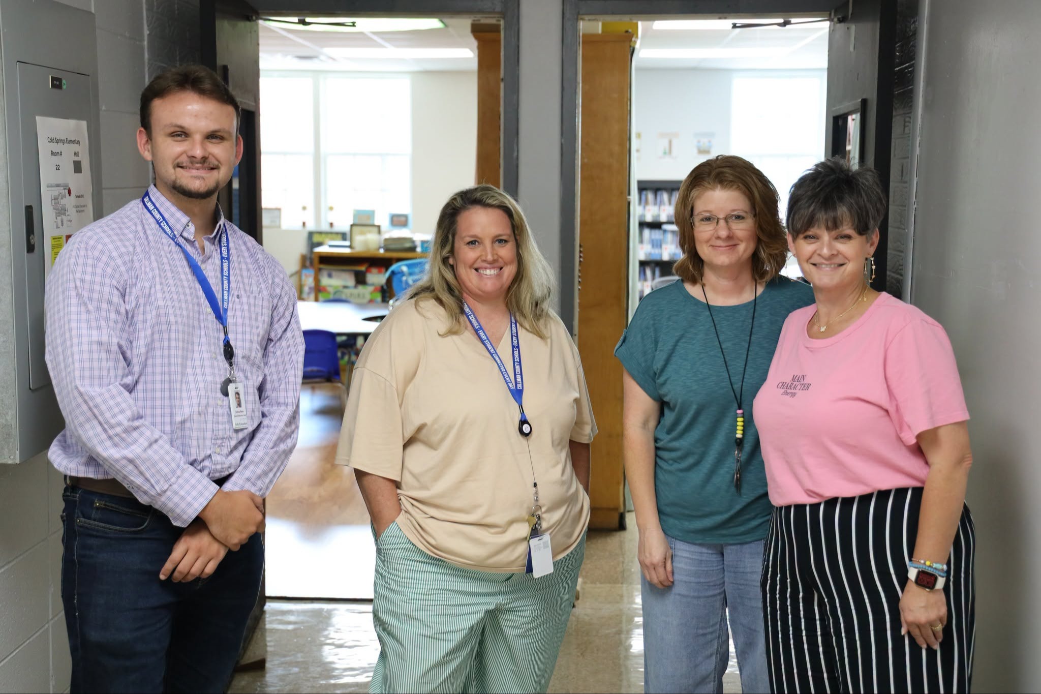 Five people in light-colored clothing and name tags pose together inside a bright, modern building.