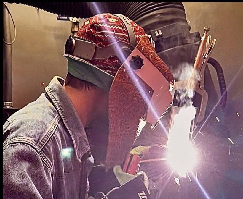 A person wearing a welding mask and gloves is welding something in a workshop.
