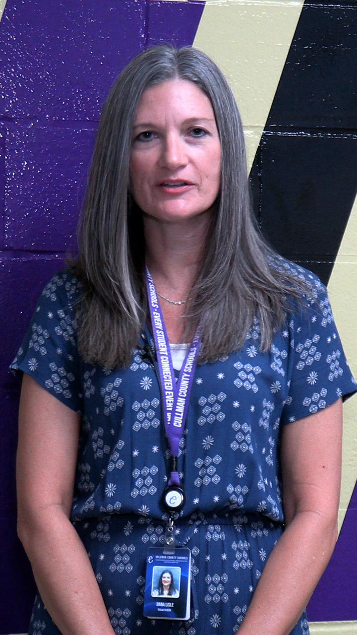 Woman in a blue dress with a lanyard around her neck. Behind her is a purple and black wall.