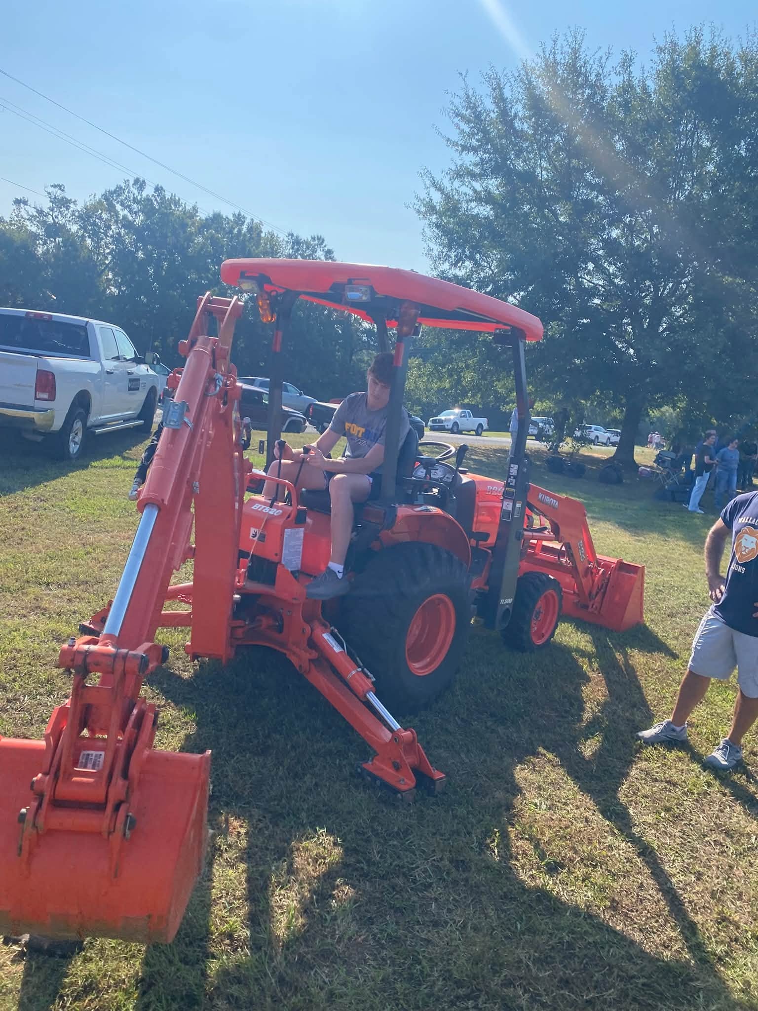 Red tractor on grass. A person is sitting in the driver's seat. A man walks by.