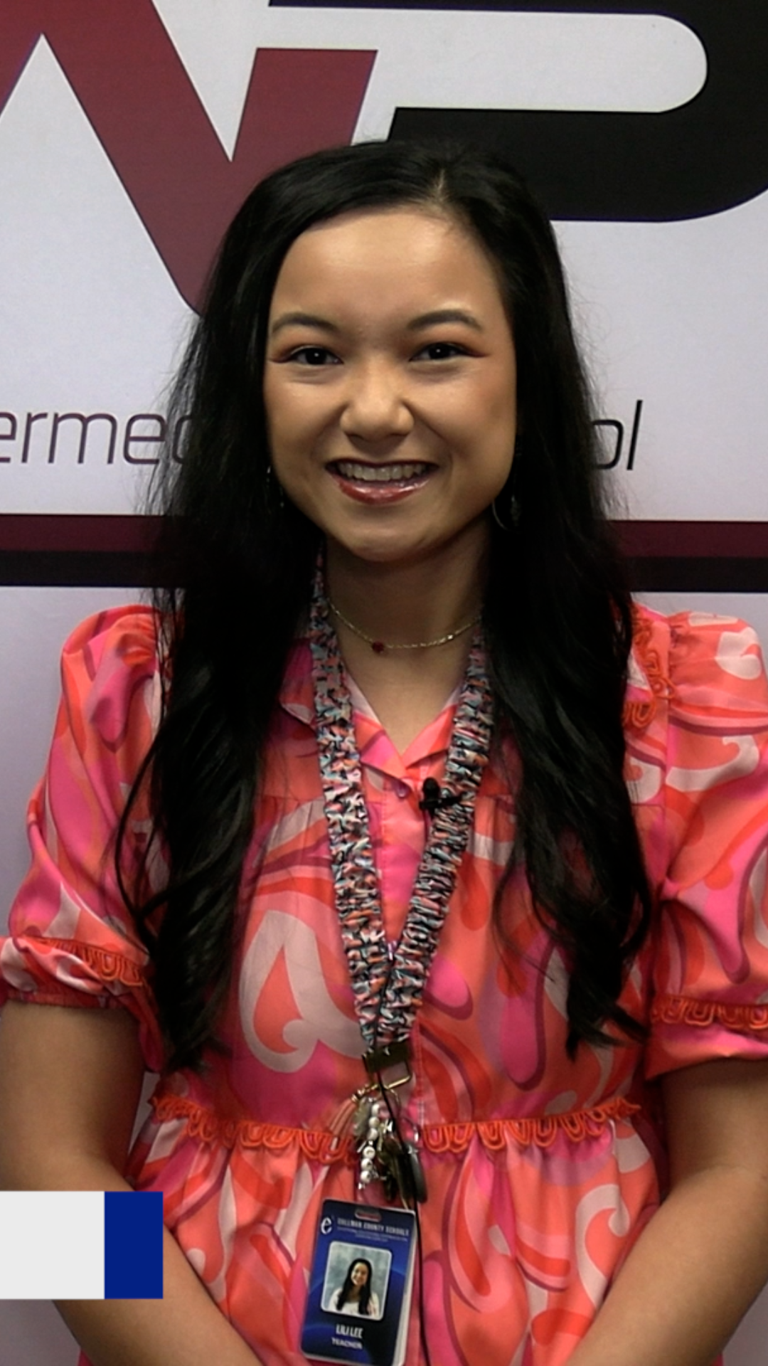 Woman wearing a pink dress and ID lanyard with an ID card with a picture of her standing against a white and maroon backdrop.