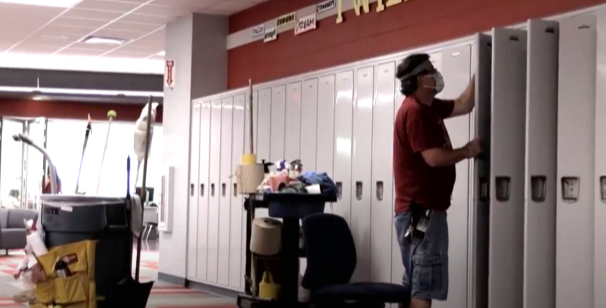 Picture of a man cleaning lockers in a school. The picture also shows cleaning supplies on a cart behind him.