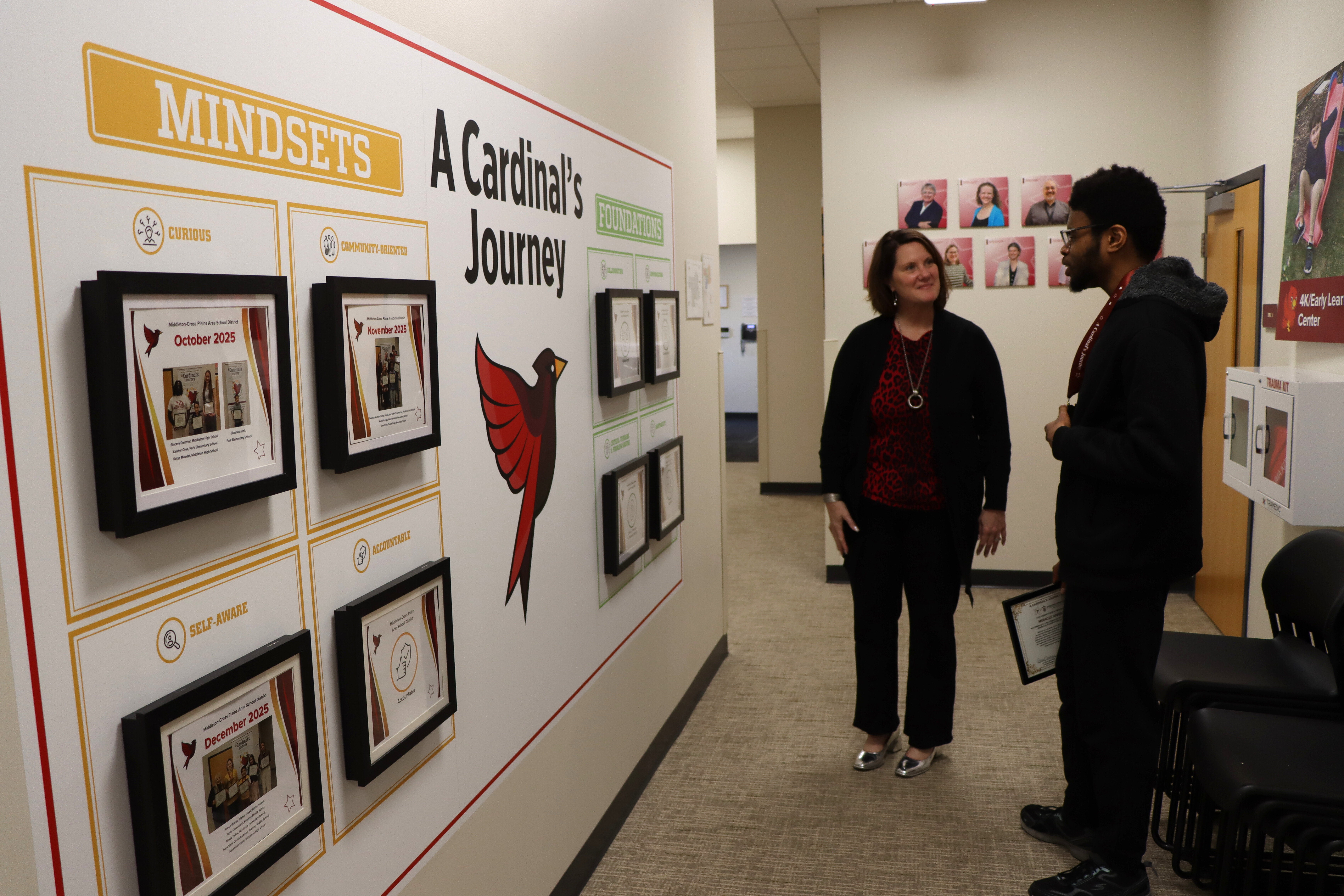 Dr. Dana Monogue smiling and standing with a student in front of the Cardinal's Journey wall mural