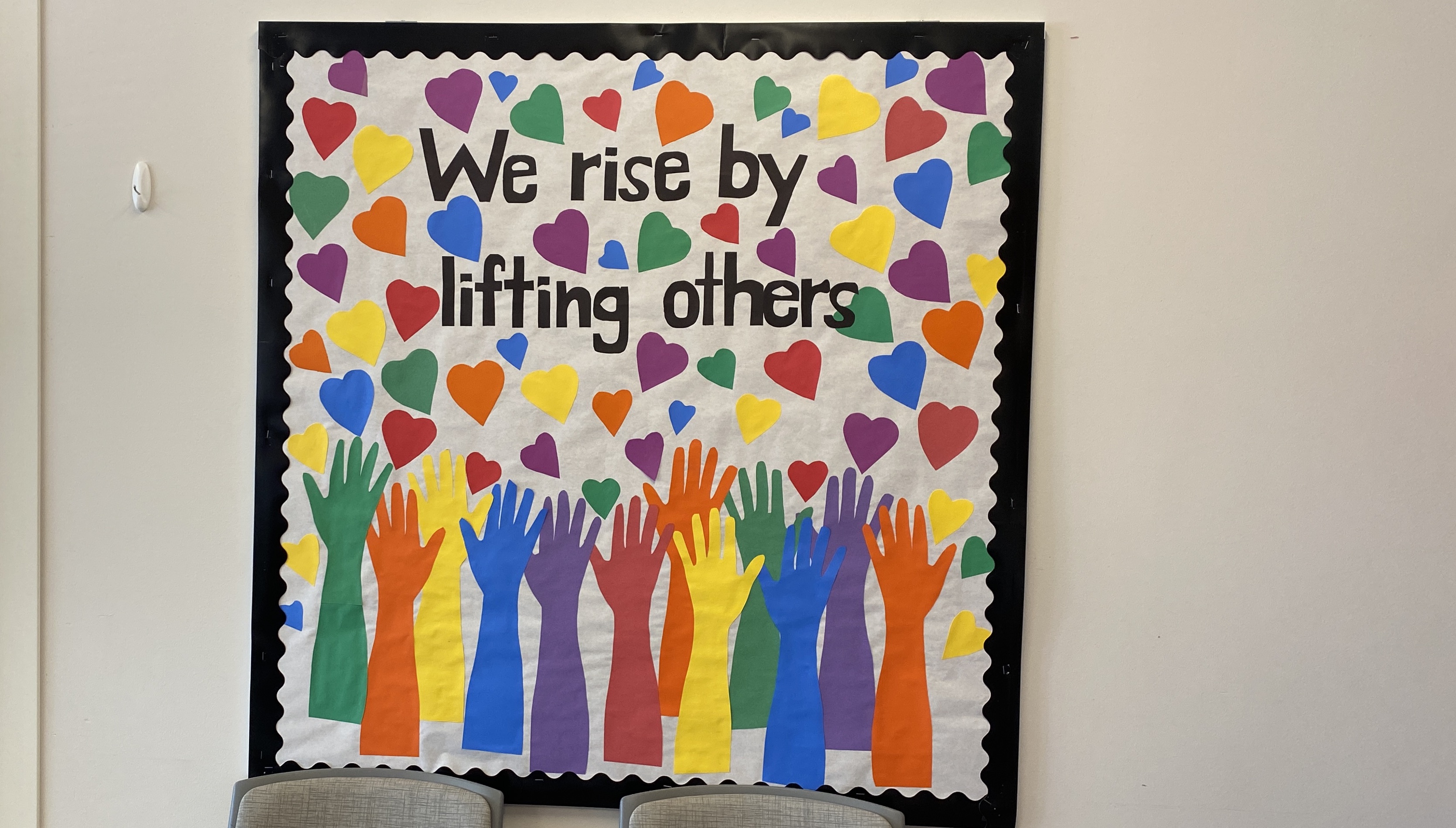 bulletin board that says "We Rise By Lifting Others."