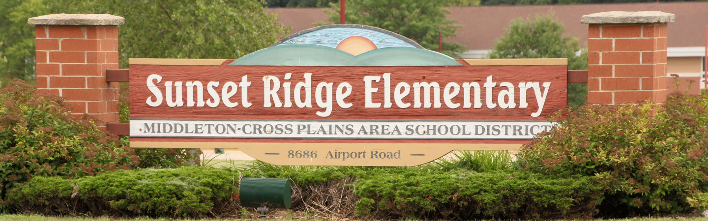 Picture of the  sign "Sunset Ridge Elementary" school sign. The sign has an image painted on it depicting green hillsides with the sun rising against a blue sky. The school address, 8686 Airport Road is included on the sign.