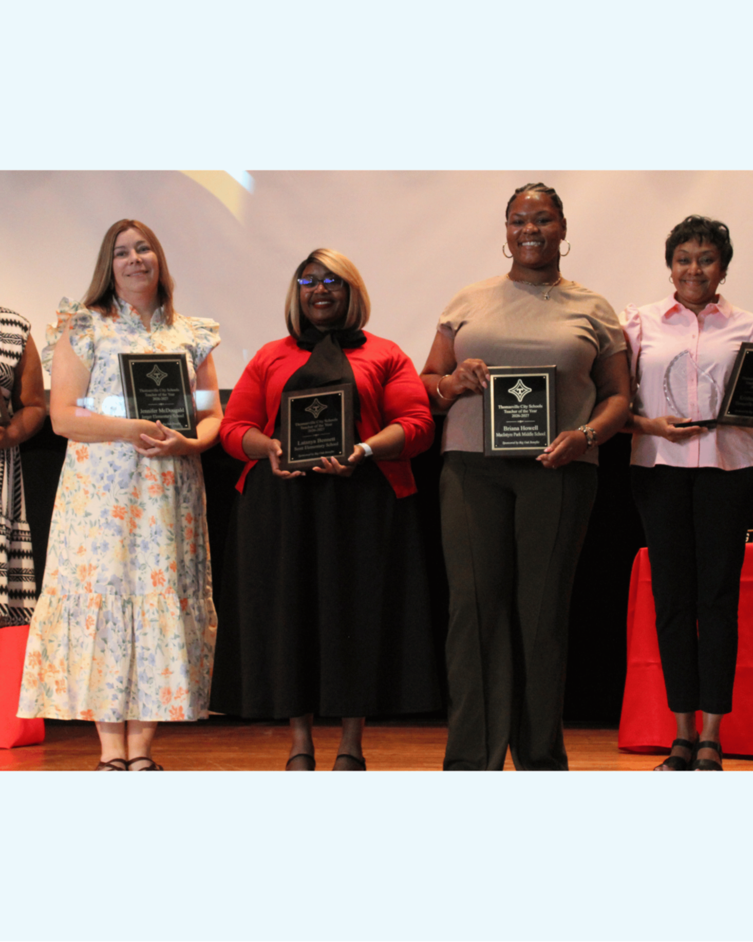 A group of women in formal attire, standing together and holding awards, likely at an event.